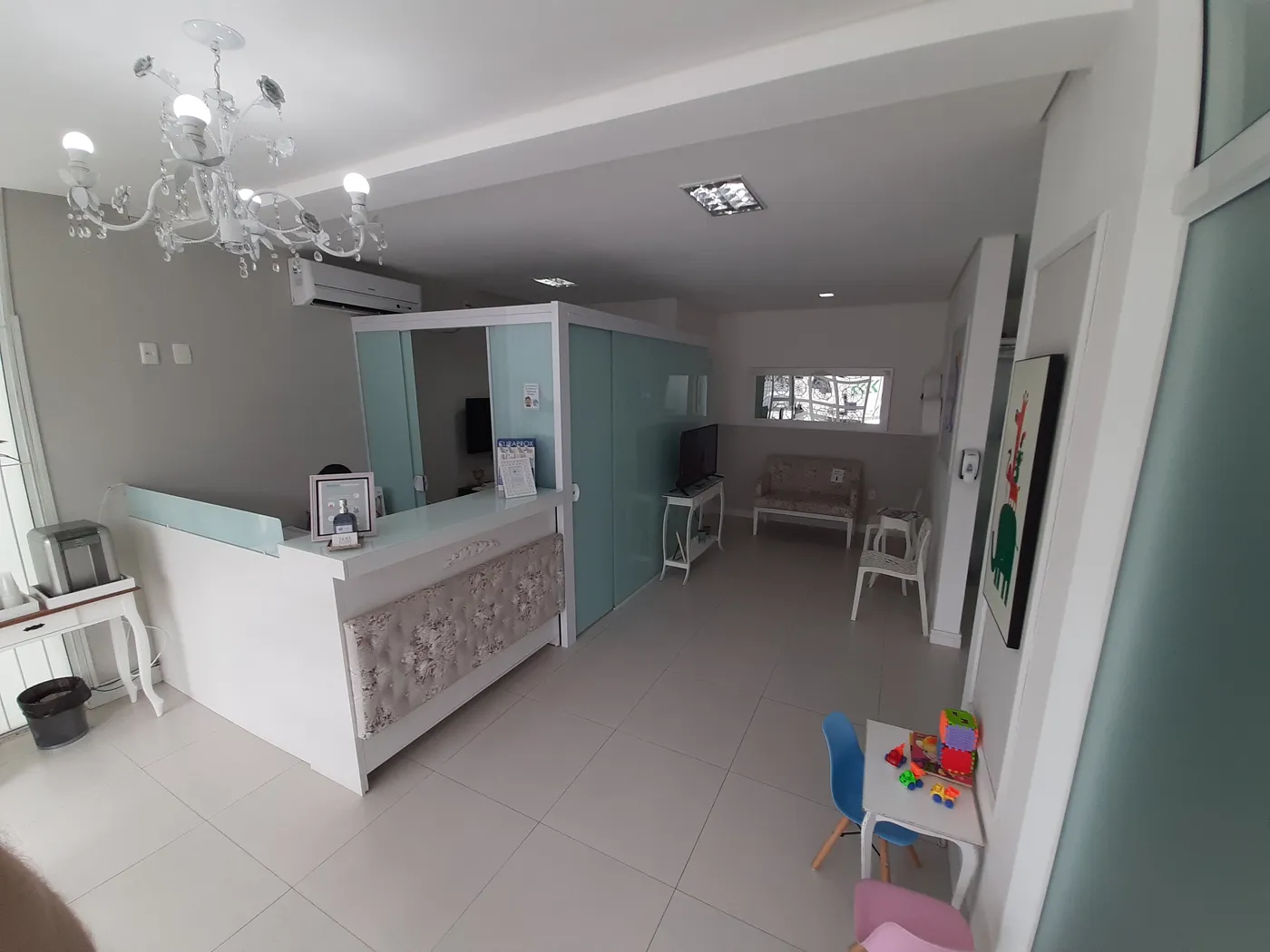 Recepção da clínica com balcão branco, lustre e mesinha infantil